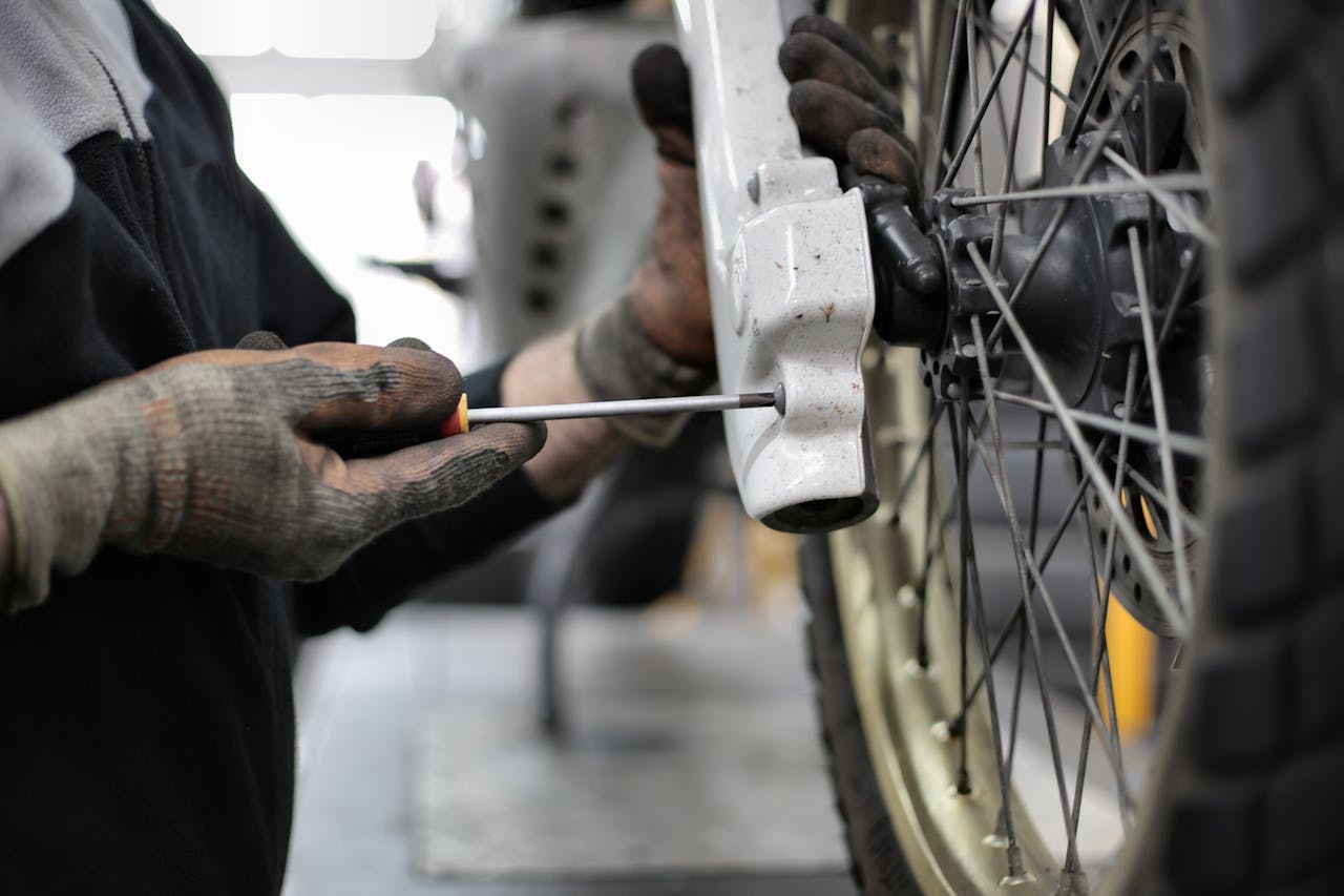 Close-up view of a mechanic's hands repairing a motorcycle wheel using a screwdriver in a workshop.